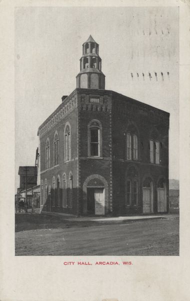 Exterior view of the front entrance on a corner of the two-story brick City Hall. A horse-drawn wagon is visible on the far left. Caption reads: "City Hall, Arcadia, Wis."