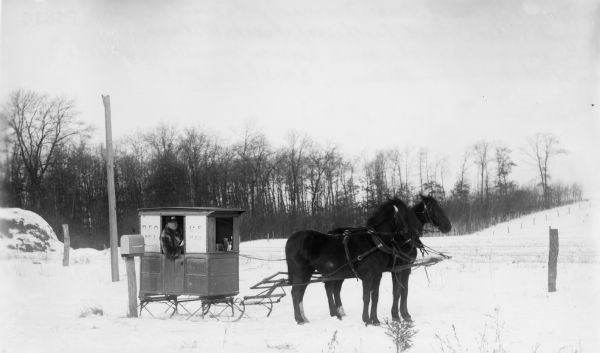 Man delivering mail in winter using a sled pulled by two horses.