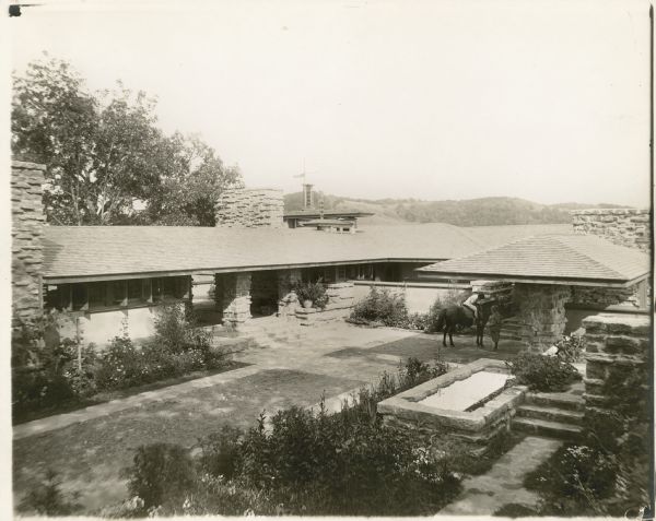 Taliesin I courtyard from the "brow" of the hill looking toward the entry loggia. A young girl on a horse is talking to a young boy under the porte-cochere.