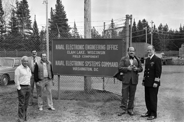 Captain Charles Biele (right) and John A. Lavine (next to Biele), Wisconsin newspaper publisher, before Lavine toured the controversial U.S. Navy facility at Clam Lake known as Project ELF. To the left of the sign is local activist Jerry Holter and two unidentified men.