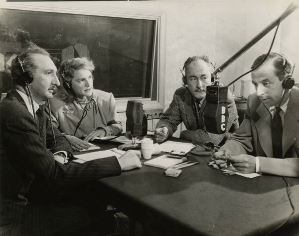 Alistair Cooke of the BBC broadcasting from the United States to the United Kingdom. On the far left is the American news commentator Cecil Brown, who broadcast the news for CBS, Mutual, ABC, and NBC.