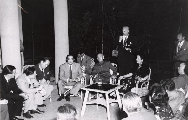 Chiang Kai Shek during a press conference shortly after his arrival in Taiwan. Seated beside him is Madame Chaing Kai Shek and standing is reporter Cecil Brown of the Mutual radio network.