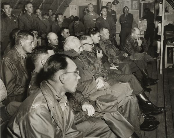 Military personnel at an early morning briefing at the First Corps headquarters in Korea. American journalist Cecil Brown is seated next to the officer in the first row who is wearing glasses and smoking a pipe. Martha Brown, who was accompanying her husband on this wartime assignment, is seated to that man's left.