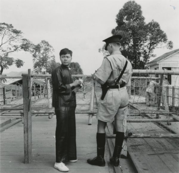 A British soldier or police officer  and a civilian on the bridge between the British area of Hong Kong and Communist China.