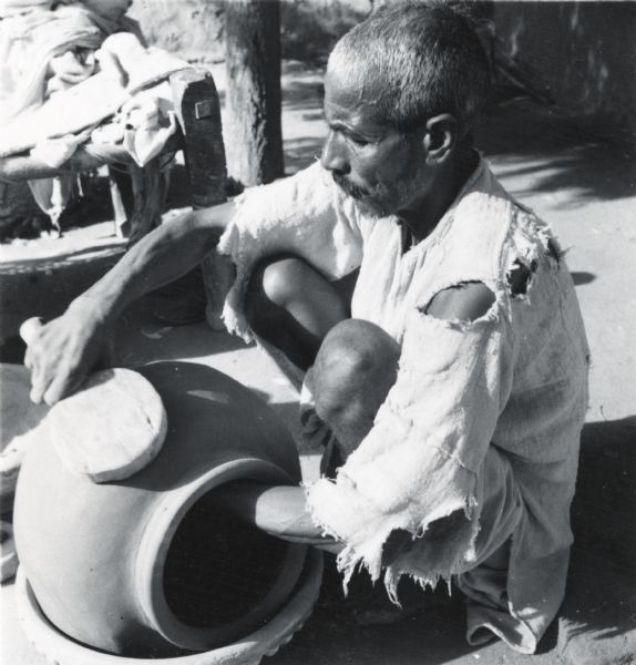 Man squatting on ground while making a large, earthenware pot in Jaipur, India.