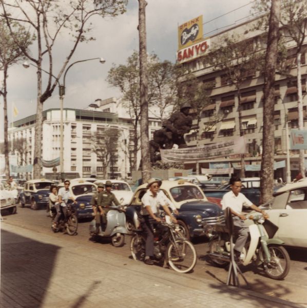 A busy street in wartime Vietnam with bicycles, motorbikes, and automobiles.