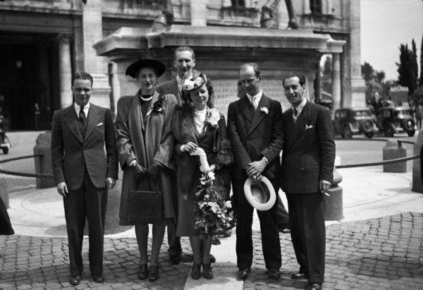The wedding of journalist Richard Scott Mowrer of the "Chicago Daily News" (hat in hand) and Rosemund Emily Cole in Rome, Italy. Mowrer had just been expelled by Mussolini for his anti-fascist articles. A few minutes before the deadline, the couple was hastily married with friends Cecil Brown, behind the bride, and Martha Brown, as witnesses.  Also in the wedding party are American consul John Jones, on the left, and a man identified as Pepino. Then, as Brown wrote in his scrapbook, the happy couple "beat it to the border."