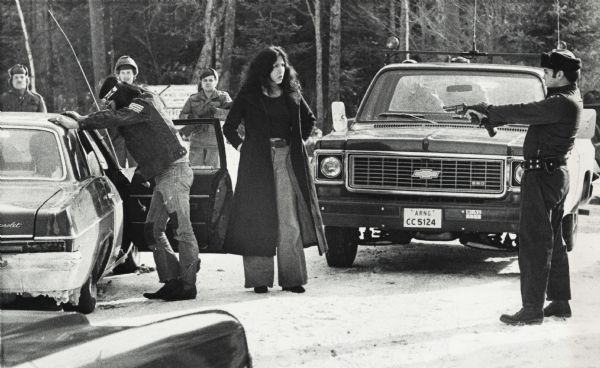An unidentified member of the Wisconsin State Patrol points his revolver at several Native Americans at a vehicle checkpoint near Gresham. The State Patrol and the Wisconsin National Guard were present because members of the Menominee Warrior Society had seized the Alexian property at Gresham. Ultimately this incident led to the arrest of the occupants of the vehicle.