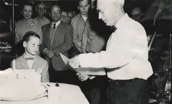 Clough Gates, publisher of the "Superior Telegram," cutting a cake to celebrate his 80th birthday. Max Lavine stands in the middle background, and watching is John Murphy, son of Morgan Murphy.