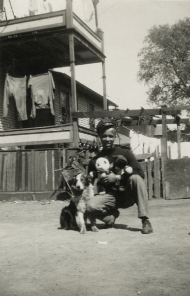 Lewis Arms poses holding stuffed toy animals, with an arm around a (real) dog. He is in the back yard of the house at 629 Milton Street.