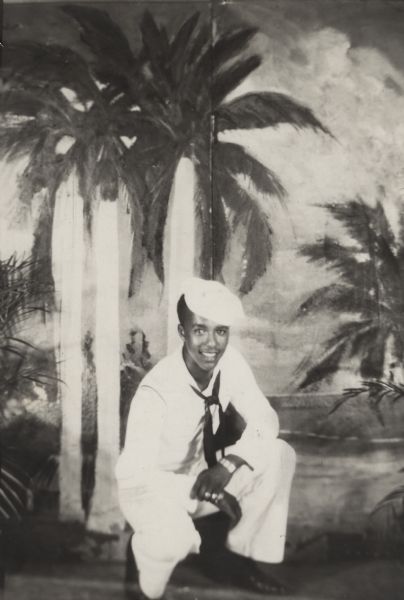 Lewis Arms poses in front of a tropical backdrop wearing his Navy uniform. There is an inscription on the back that reads, "Love to Mom from your loving son Lewis. U.S. Navy".