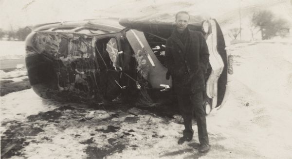 Lewis Arms stands next to a damaged 1946 Chevrolet which had been rented from Friede Rent-A-Car. Arms and Bert Rogers had been traveling to Milwaukee in the car when they rolled it.