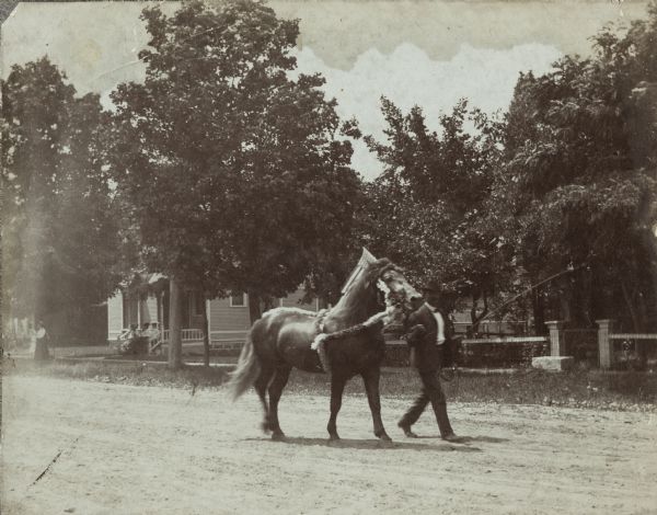 Charles Steppe, the biological father of Lewis Arms, leads a horse down a street. The horse is wearing an ornate bridle and they may be in a parade.
