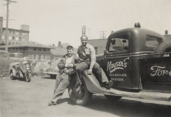 Bill Mootz (left) and Lewis Arms pose with a truck that advertises "Kayser's, 702 E. Wash. Ave., Madison" on the door. Both men were employees at Kayser Motors. In the background is a three-wheeled motorcycle.