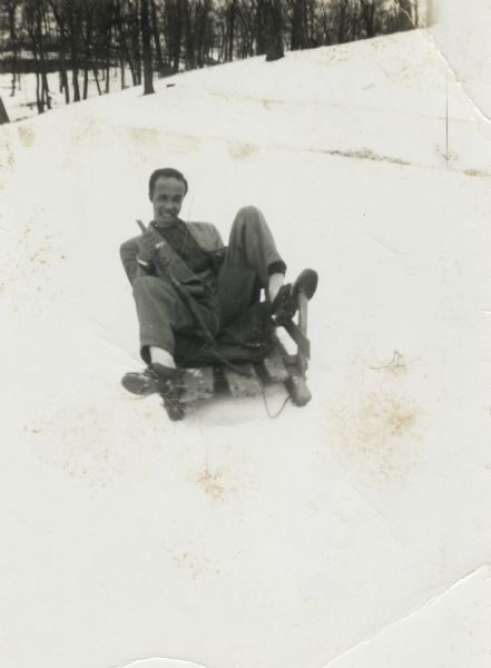 Winter scene with Lewis Arms sitting on a sled in the snow at his uncle Otis Arms's farm, Hillsboro (Vernon Co.), Wisconsin.