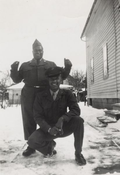 Lewis Arms (kneeling), who is wearing his Marine Corps uniform, poses with his first cousin Chester Elvord, who is wearing his Army uniform. They are on Lake Street outside of a house.