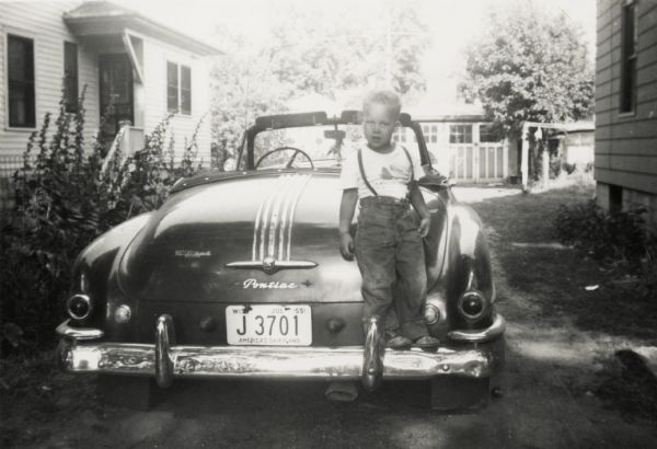 Lewis Arms Jr. poses on the back of his father Lewis Arms's 1949 Pontiac convertible automobile.