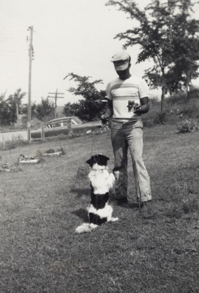 Lewis Arms plays with his dog Tuffy. He is wearing his Marine Corps hat, and his automobile is visible parked in the background.