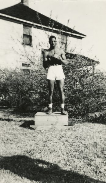 Buddy Brown poses outdoors standing on a box wearing boxing gloves and trunks.