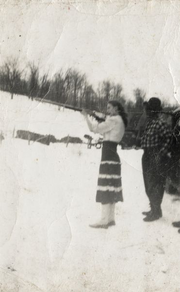 Elinora (mother of Lewis Arms, Jr.) stands in the snow and shoots a rifle, while Walter Arms, uncle of Lewis Arms, looks on.