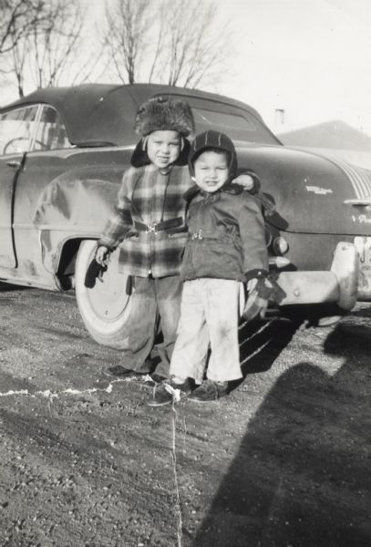 Lewis Arms, Jr. (left, in a fur hat) poses in front of a Pontiac automobile with his arm around his younger brother Craig Arms. They are on Beld Street.