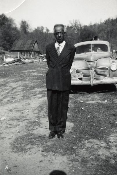 Otis Arms, uncle of Lewis Arms, poses in front of an automobile. He is dressed in a suit.