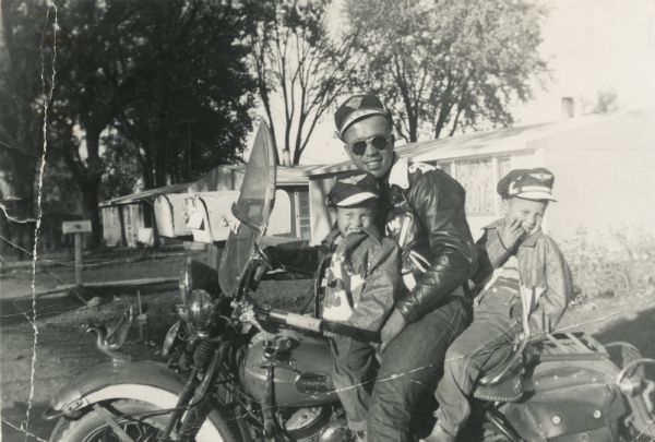 Lewis Arms is seated on his motorcycle with Craig Arms sitting in front of him and Lewis Arms, Jr. behind him.