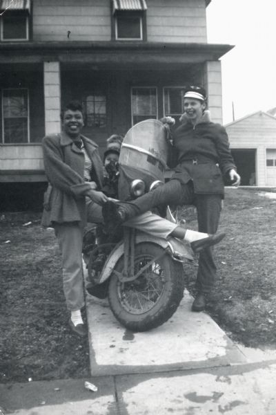 Friends Connie Moore (left) and LuRay (Frenchie) Arms pose comically with a motorcycle at 1851 South Park Street. Two children can be seen behind them sitting on the motorcycle.