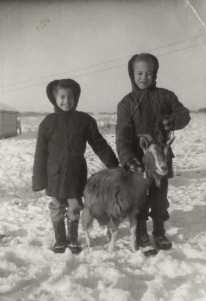 Craig Arms (left) and his brother Lewis Arms, Jr. pose with a goat, standing in the snow.