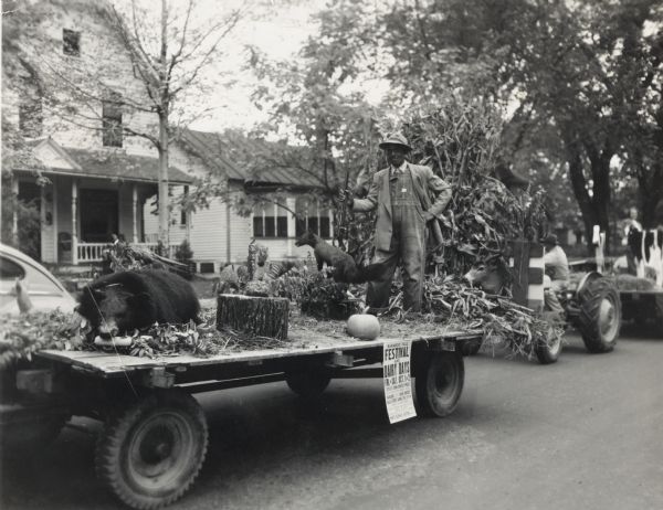 Bernard Arms holding a firearm poses on a parade float decorated in an autumn theme, including a stuffed bear, fox, and squirrel. The parade was a part of a Baraboo Fall Festival and Dairy Days celebration.