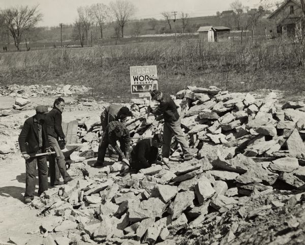 National Youth Administration workers cutting stone in the quarry near the Grignon House. A sign behind the group of boys says: USA Work Program."