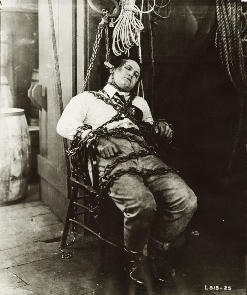 Harry Houdini, world famous escape artist who spent his boyhood in Appleton, Wisconsin, sitting in a chair wrapped in chains in a scene from the silent film "Terror Island." The film featured several of his escapes.