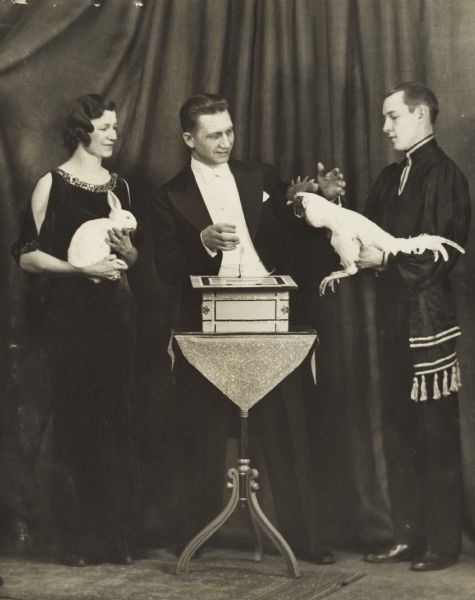 Magician Ben Bergor of Madison performing a trick on stage. With him are his wife, who performed as Madame Alva, and an assistant.