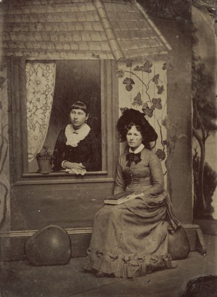 Tintype of Estella Moessner Goldenberger of Madison, (in the window), with her friend Celia Gibson posing in front of a painted backdrop.