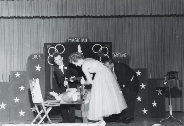 Professional magician Dick DeYoung of Sheboygan, Wisconsin, on a stage with three other people. DeYoung had over five decades of experience as a club and stage magician.