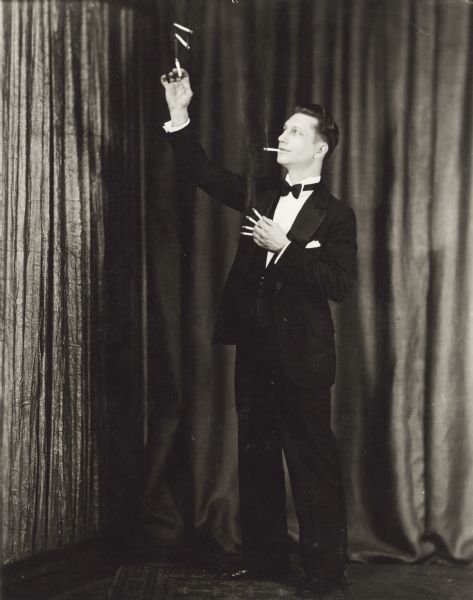 Formal publicity portrait of magician Ben Bergor of Madison performing one of his sleight of hand tricks with lighted cigarettes. Bergor was billed as the fastest hands in the business.