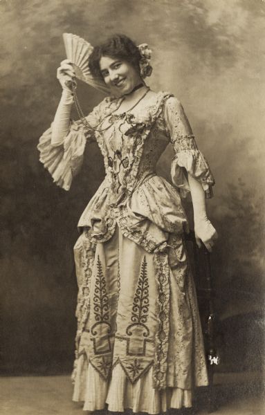 Olivia Monona wearing a costume worn as a chorus member of the Chicago Opera. The image is a photographic postcard she sent to Oscar Hanke, a violinist with the company, and who later became her second husband. Olivia Monona was the stage name for Olivia Goldenberger who was born in Madison and graduated from the University of Wisconsin.
