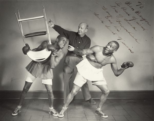 The Gold Dust Twins were a popular comedy-musical act that toured in the Midwest during the 1950s. The two men sang, danced, and performed banjo music, as well as boxing three rounds. George Moorhead served as the referee for this performance. The twins are not named in their promotional literature. The photograph was autographed for Ben Bergor, a Madison magician and theatrical agent, who was their exclusive agent at one time. The twins were named after the Gold Dust Twins, mascots for a dishwashing soap popular at the turn of the twentieth century.  The phrase came to mean any two talented individuals who worked closely together, especially in sports.
