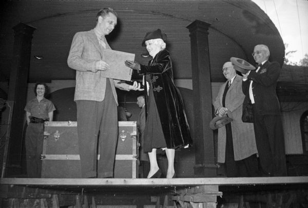 Ben Bergor, a Madison magician, receiving the Houdini Award from the widow of Harry Houdini. Behind him is the trunk from which Bergor had escaped, and four unidentified individuals. Bergor had previously won the Houdini award, and with this escape he was awarded permanent custody of the award.