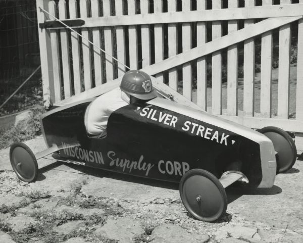 Thirteen year-old Philip Lenhart of Madison, Wisconsin, sitting in his new and improved soap box derby car. In the 1950 Madison race held on July 23, 1950, Philip was the runner-up in the class A division (13-15 year olds) and won a sports jacket from Olson & Veerhuseun men's clothing store.