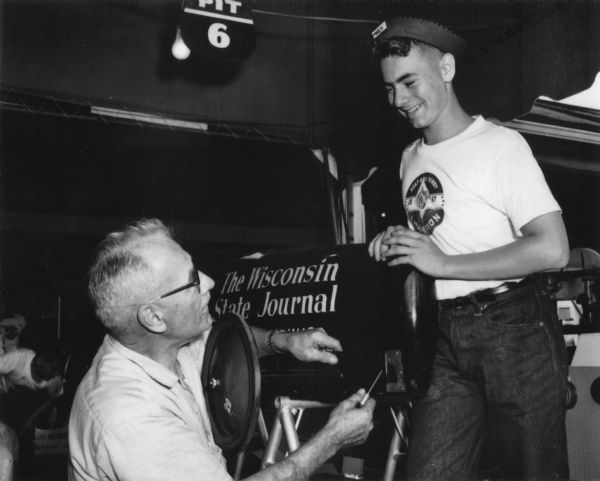 Van Steiner (15 years-old) of Argyle, Wisconsin, the 1957 Madison, Wisconsin soap box derby champion, working on the steering of his Wisconsin State Journal-sponsored car at the All-American Soap Box Derby, Derby Downs, Akron, Ohio, along with a derby volunteer.