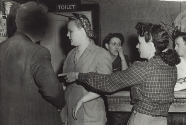 A state agent arrests three women and one man, a bartender, in Jeanne's Chateau. A sweeping raid was staged on many Hurley area establishments. The arrest warrants were for gambling and prostitution. The agent's face is blocked out.
