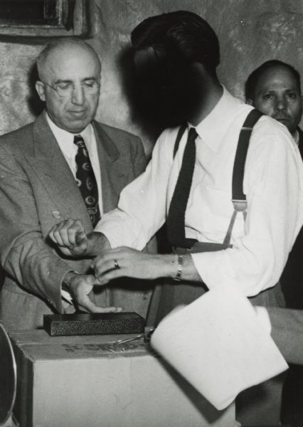 John M. Califano, operator of the Blackhawk Bar, as he was fingerprinted on Wednesday by FBI agent (face blacked out) at the Iron County jail, following a sweeping raid on many Hurley area establishments. The arrest warrants were for gambling and prostitution.