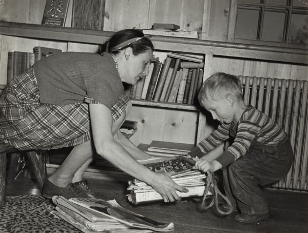 World War II permeated every aspect of life in America during World War II, and nothing was wasted that could contribute to the war effort.  Here a young boy helps his mother tie-up newspapers for collection.  The photograph was taken as part of a public relations campaign organized by the Advertising Women of New York to encourage participation in patriotic activities.