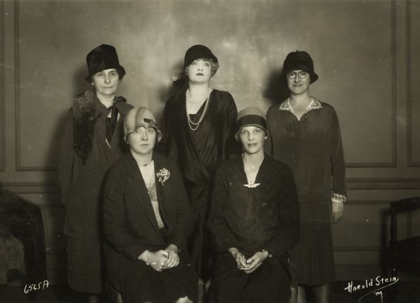 Amelia Earhart (first row, right), the speaker for a meeting of the Advertising Women of New York. Elsie Wilson, president of the club is seated next to her. Others in the photograph who also spoke: Row 2: Mrs. M. King, expert on gardens; cartoonist Grace Dayton, and Adele Bildersee, acting dean of Brooklyn division of Hunter College. Notice the special winged pin that Amelia Earhart is wearing.