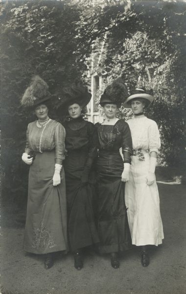 From left to right are Emma (Thorsen) Purchas (1862-1944), Ida Fisk, Ethelinda (Thorsen) Johnston (1856-1947) of Milwaukee, Wisconsin, and Dorothy Purchas (b. 1891), on vacation in Bad Kissingen. At this time Emma and Dorothy resided in England.

Wearing dresses, hats and gloves, the ladies are posed outdoors in front of trees and a trellis. Each one is lifting up her dress showing her left shoe.