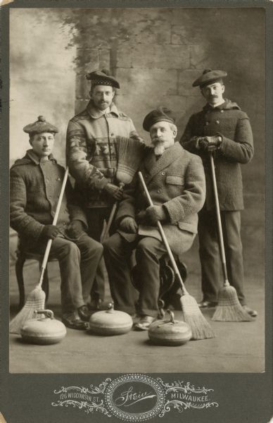 Studio portrait in front of a painted backdrop of John Johnston (1836-1904), a successful Milwaukee banker, seated second from right, with three other curling team members dressed in winter coats and hats and holding curling equipment.<p>Johnston was a member of the Milwaukee Curling Club and served as president of the Grand National Curling Club of America from 1877-1879.</p>