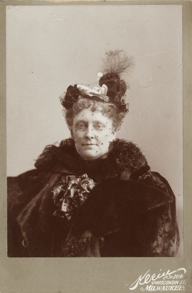 Cabinet card portrait of Ethelinda (Thorsen) Johnston (1856-1947), wife of John Johnston (1836-1904), a successful Milwaukee banker. She is wearing a seal skin coat with a bow at her neck, an ostrich feather boa, and an elaborate hat with veil.