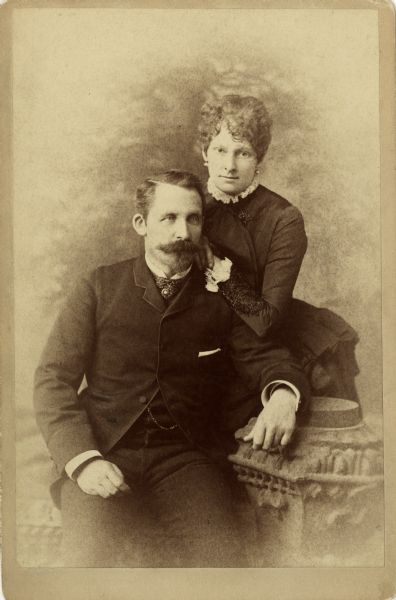 Cabinet card studio portrait of John (1836-1904) and Ethelinda (1856-1947) Johnston sitting on a decorative wall in front of a painted backdrop of trees.  John, a successful Milwaukee banker, married his second wife, Ethelinda Thorsen, on September 1, 1881.
