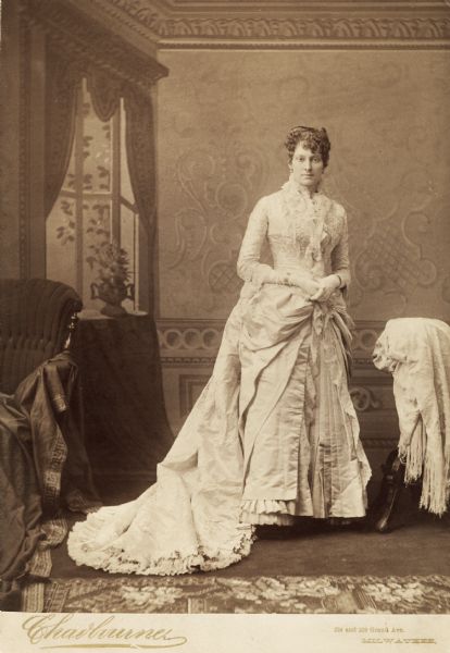Full-length studio portrait in front of a painted backdrop of Ethelinda Marie (Thorsen) Johnston (1856-1947) in her wedding gown. She was married in Milwaukee on September 1, 1881 to John Johnston (1836-1904), a Milwaukee banker, as his second wife.